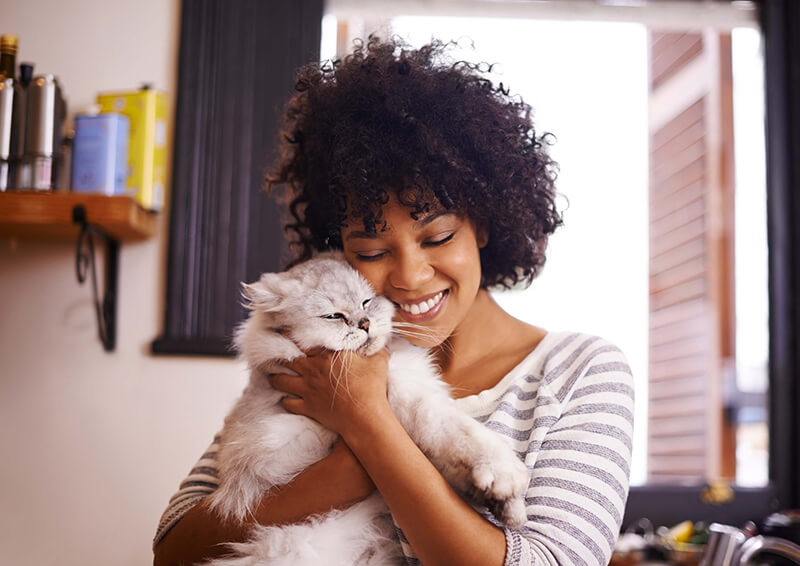 Une femme souriante aux cheveux bouclés tient un chat blanc dans ses bras.